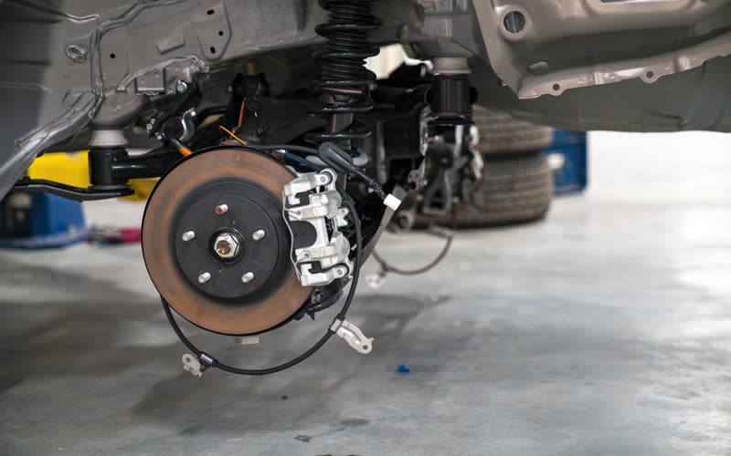 A brake disc and caliper exposed with the road wheel removed, car up on a lift