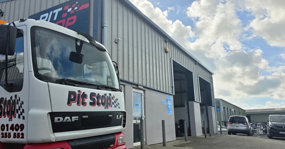 The Pit Stop Garage unit on the Holsworthy industrial estate, with the Pit Stop sign on the end wall, two roller shutter doors open and the blue MOT testing sign beside the entrance door