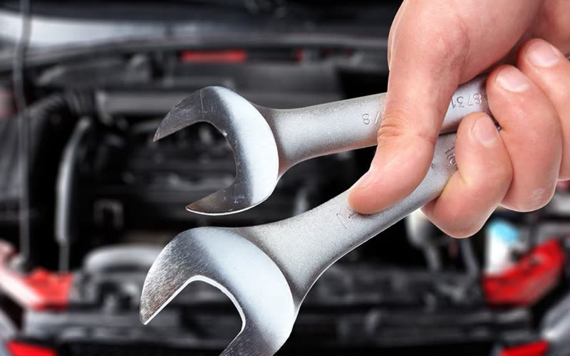 A mechanic reaching into an engine bay with a spanner during a service